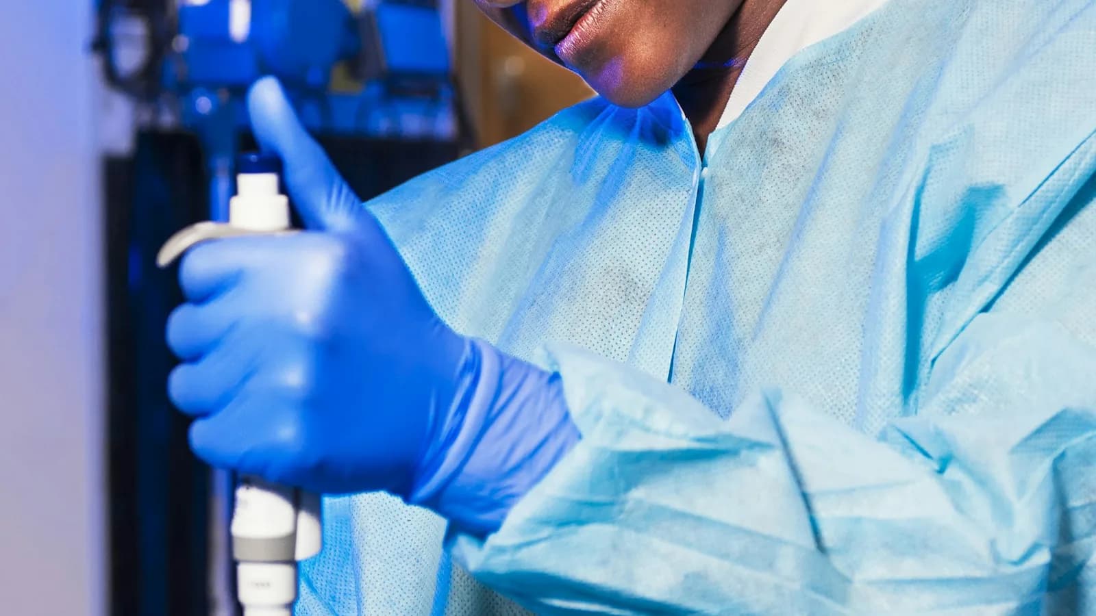 A scientist in gown and gloves using a pipette at the bench