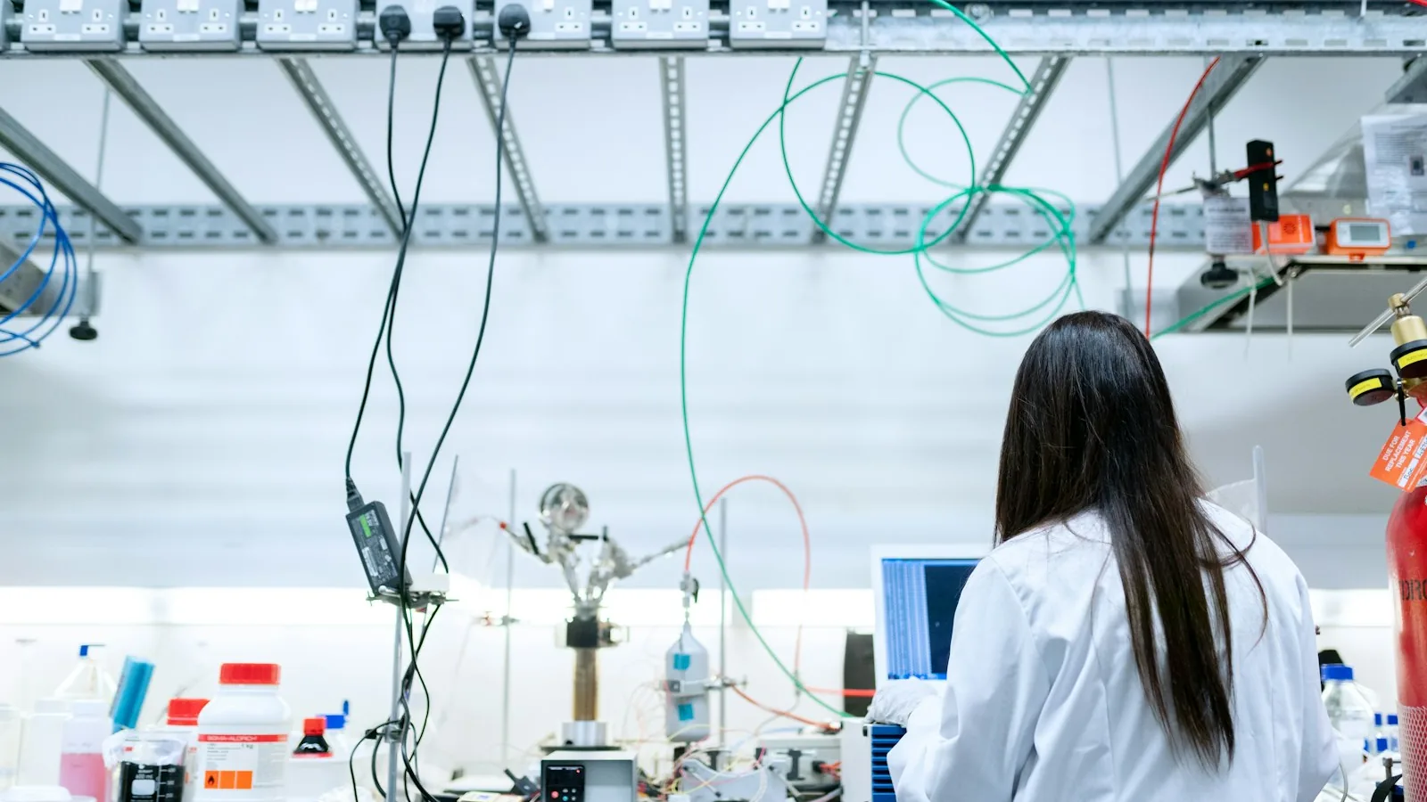 A researcher at a laboratory bench beside a screen and reagents